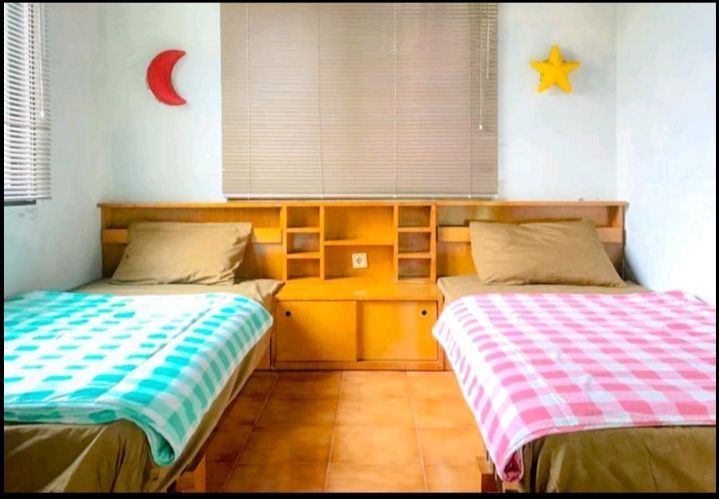 Twin beds in a room with a wooden headboard, turquoise and pink checkered blankets, and a moon and star decoration.