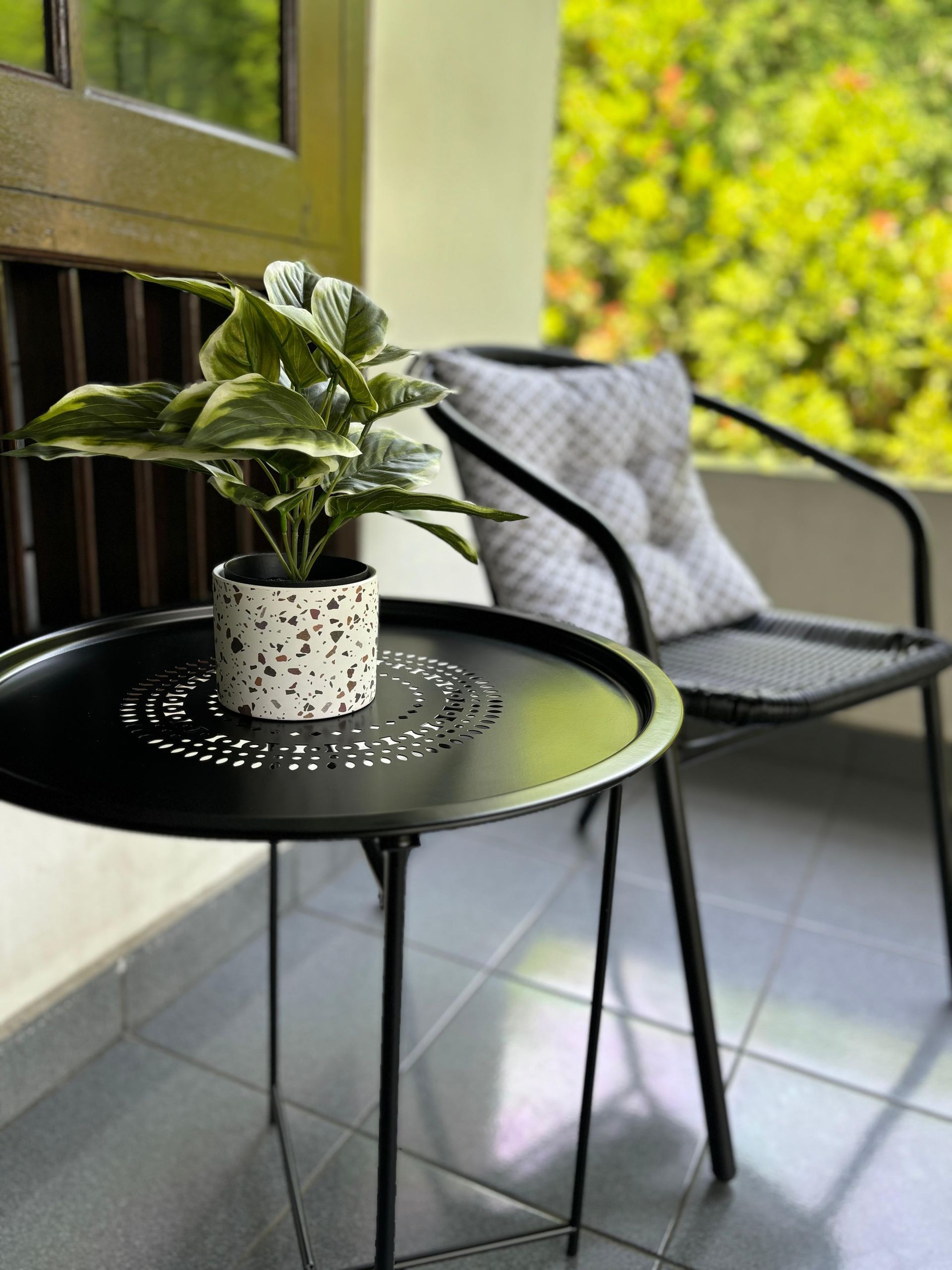 Black table with potted plant next to a chair with a cushion on a patio.