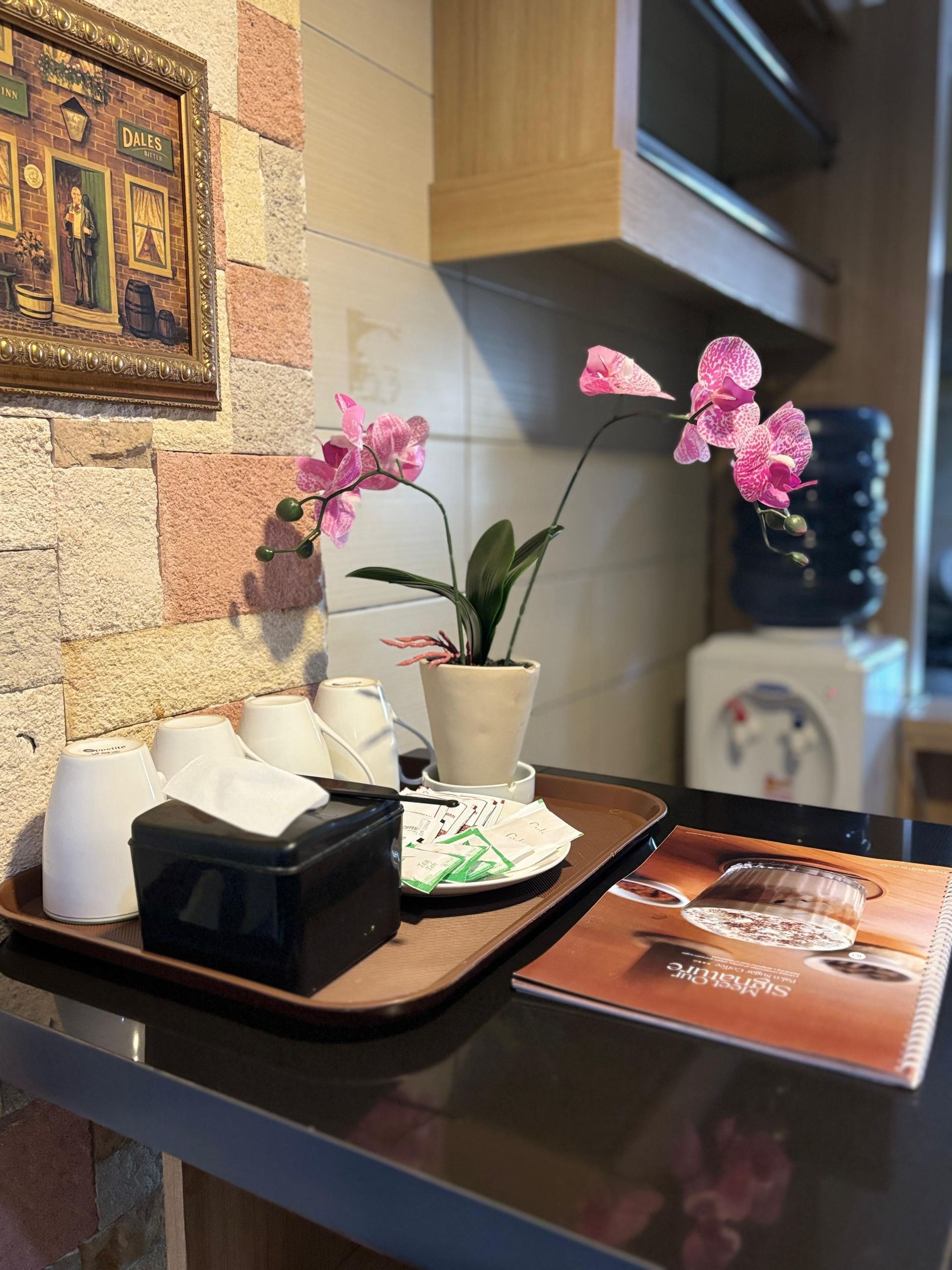 Tray with cups, flowers, tissues, and a magazine on a counter near a water cooler.