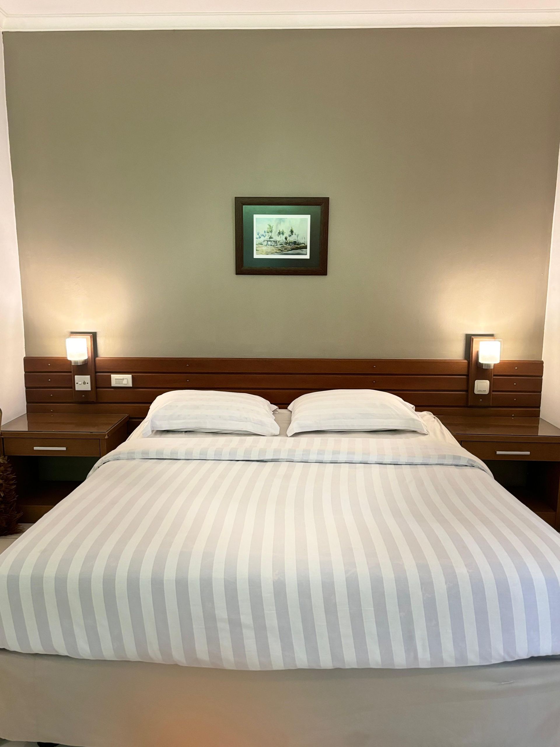 Bedroom with a bed, nightstands, lamps, and a small framed picture on the wall. The bed has striped linens.