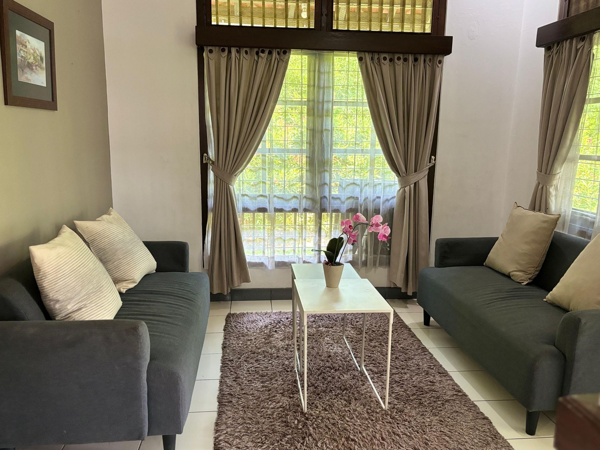 Living room with two gray sofas, beige curtains, white table, and a brown rug.