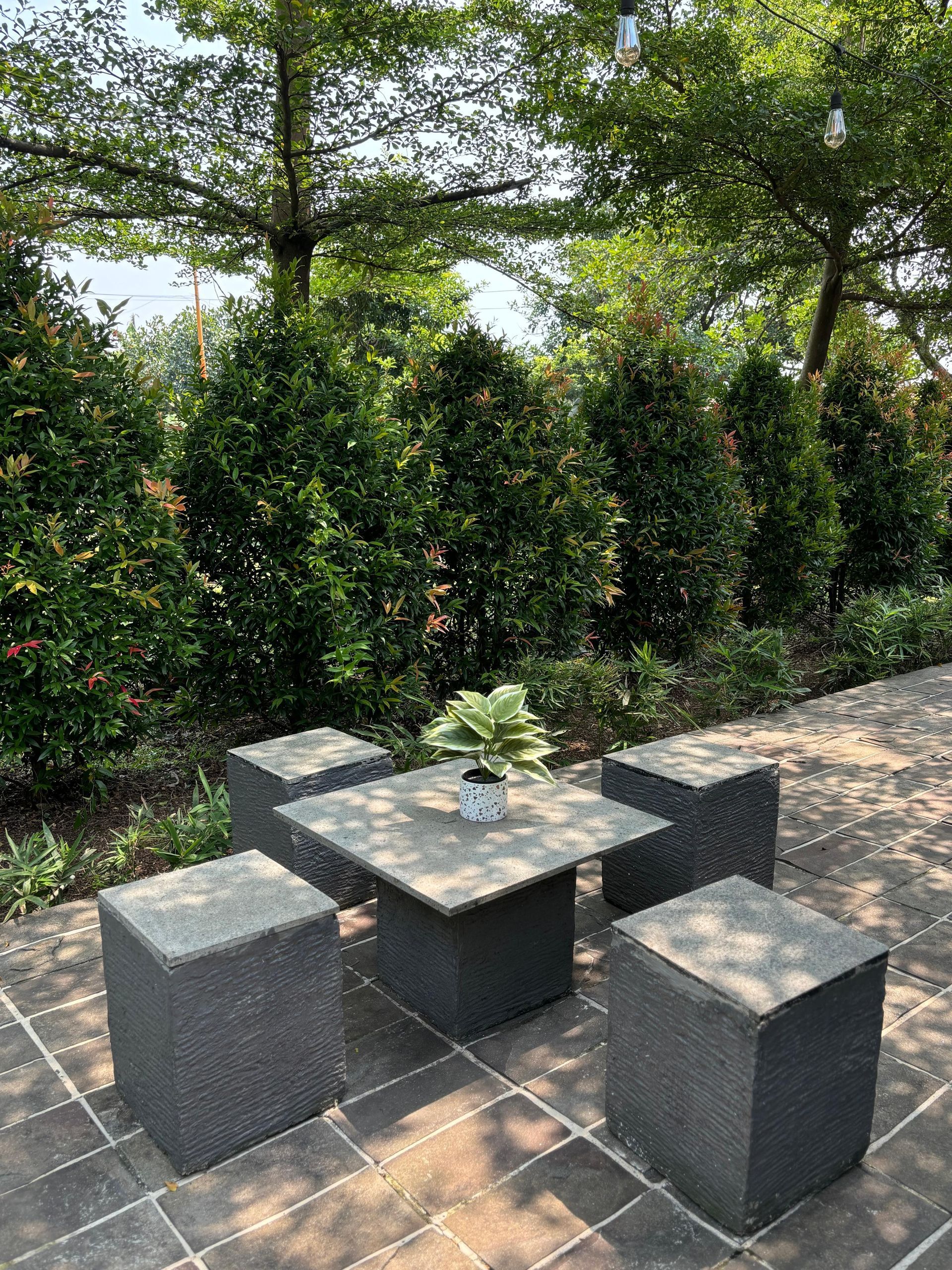 Outdoor seating area: square stone table with four matching cube seats, surrounded by greenery.
