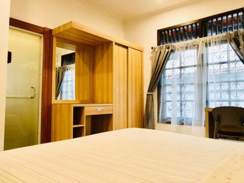 Bedroom with wooden wardrobe, window with curtains, bed. Door to left.