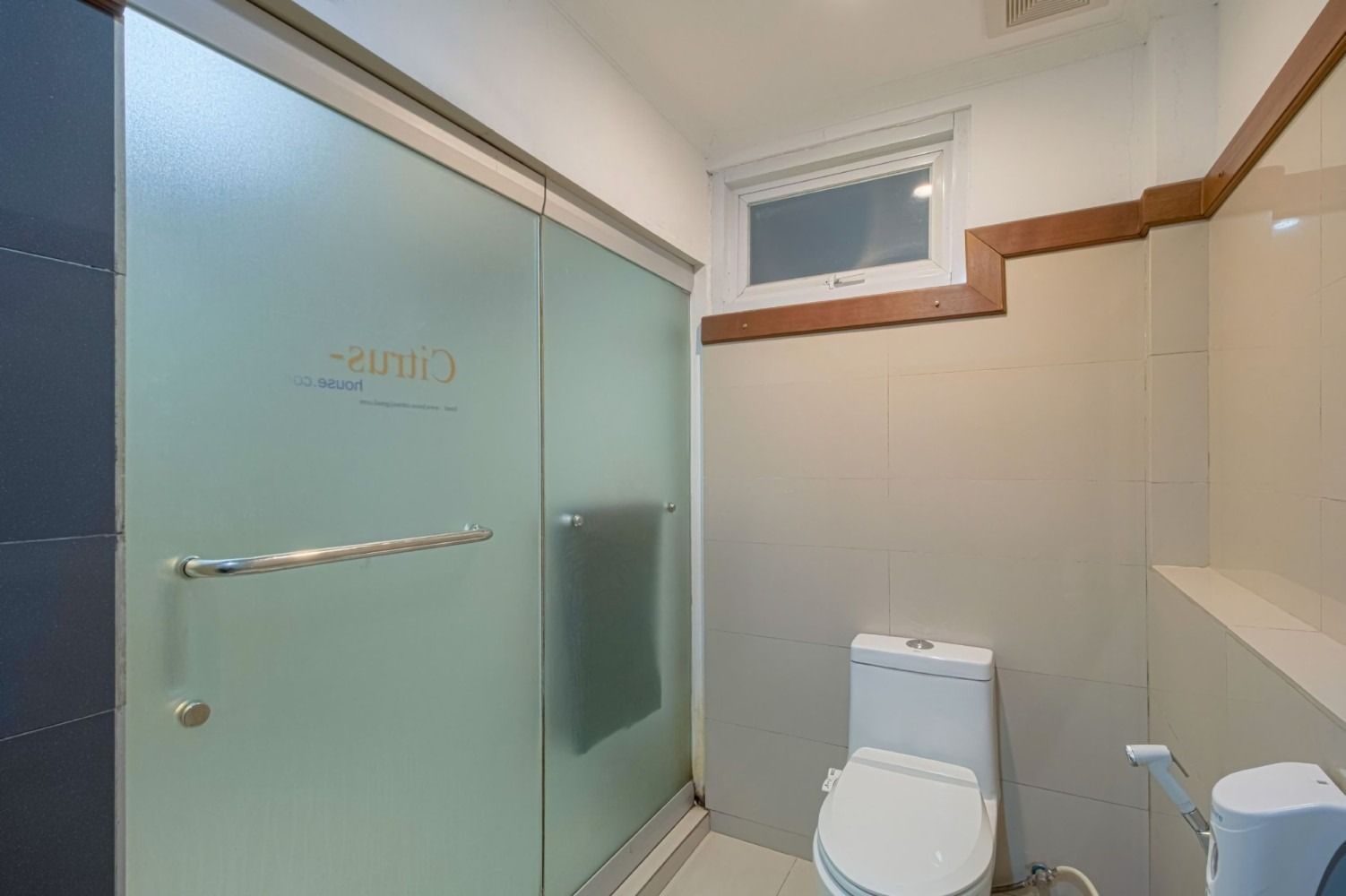 Bathroom with a glass shower door, toilet, and small window. Neutral tones, light wood trim.