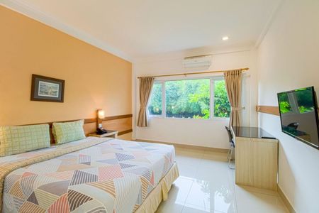 Bedroom with bed, desk, and TV; window with outdoor view, orange wall.