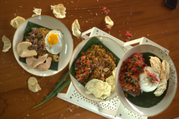 Three plates of Indonesian food on a wooden table. Each has rice, meat, and crackers; one has a fried egg.