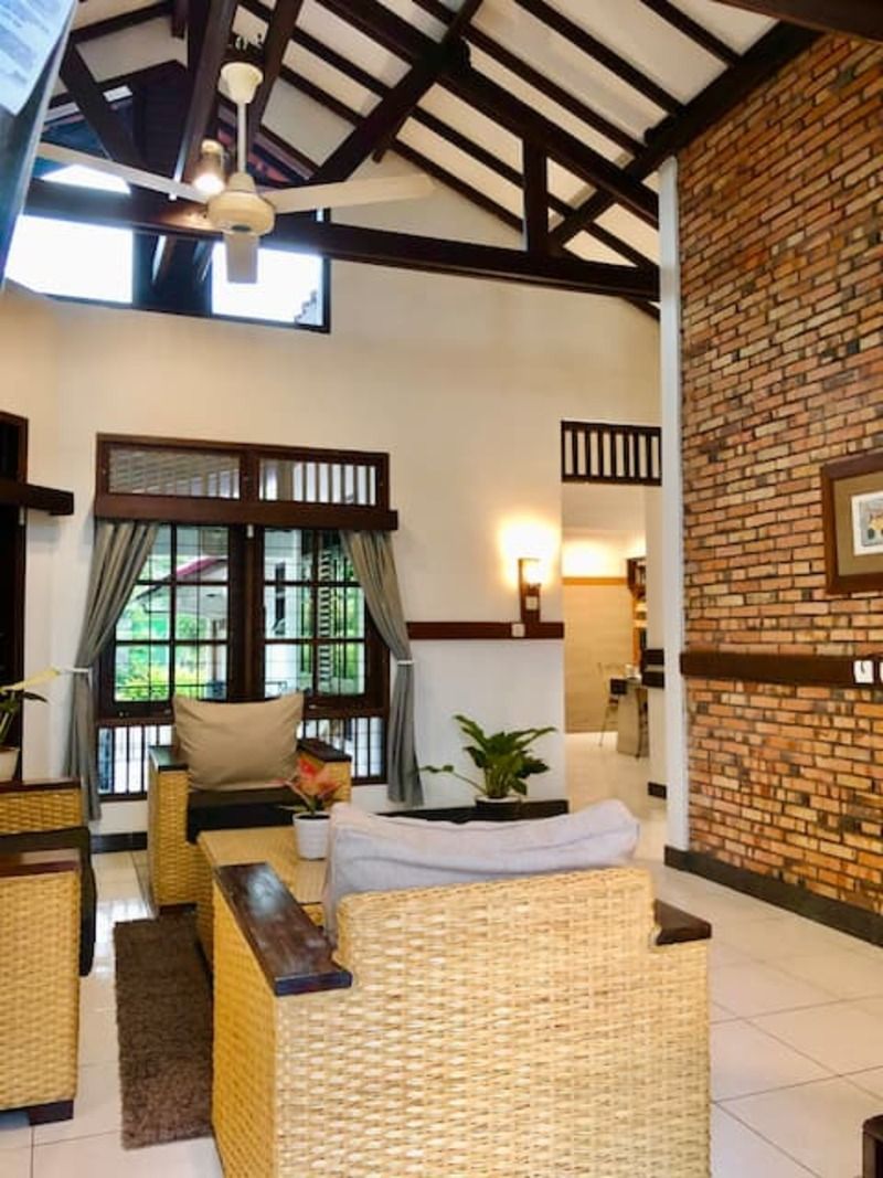 Living room with wicker furniture, brick wall, and high ceiling with exposed beams.