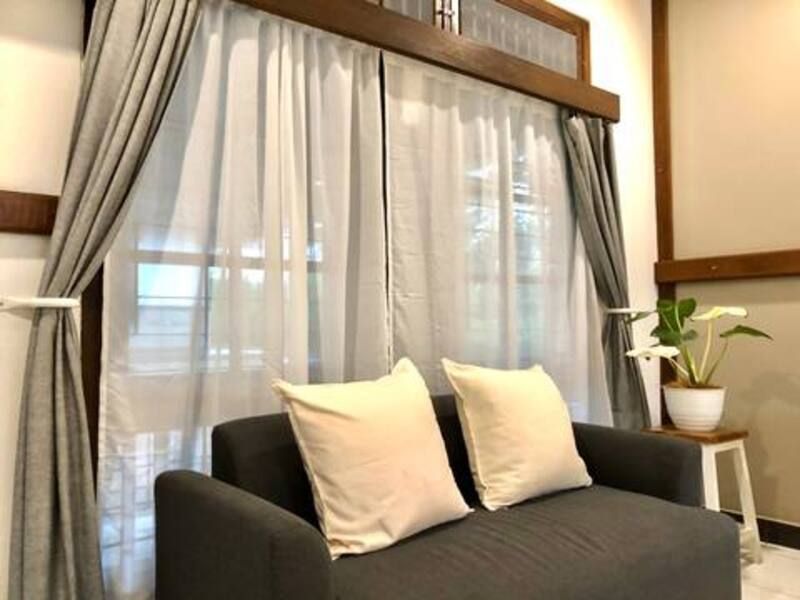 Gray sofa with cream pillows under sheer white curtains in a room.