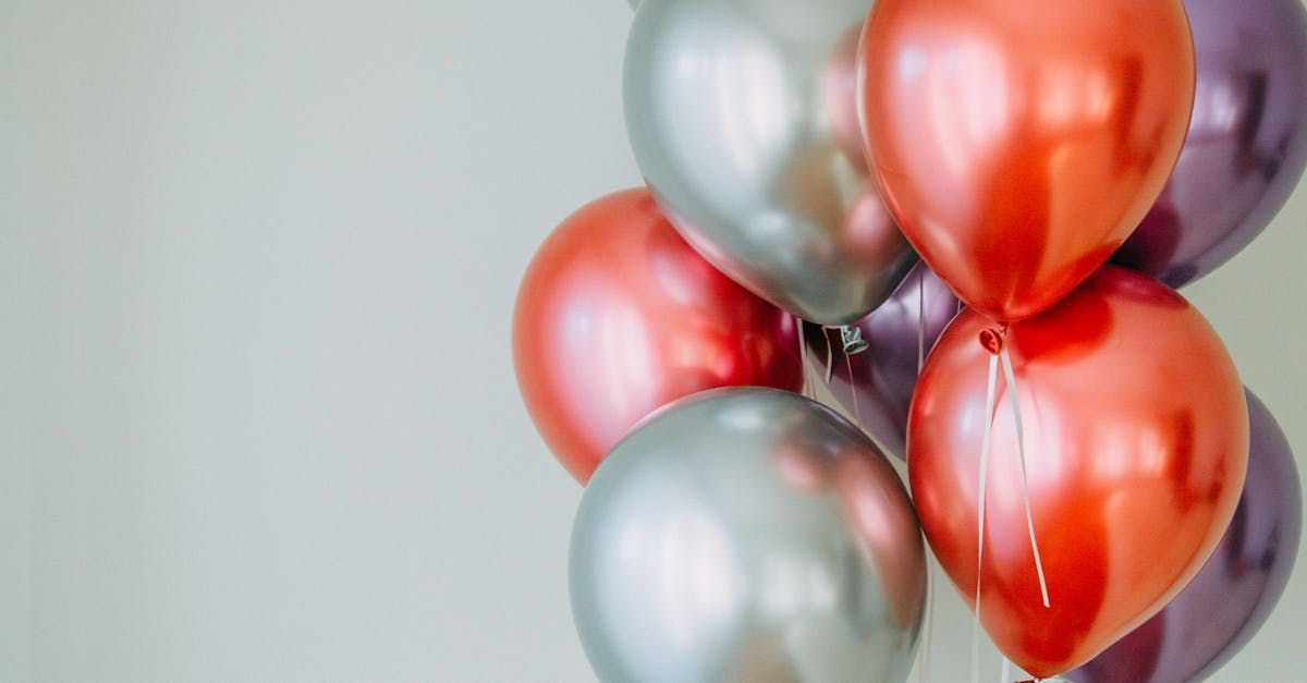 Balloons in metallic silver, red-orange, and purple against a plain light background.