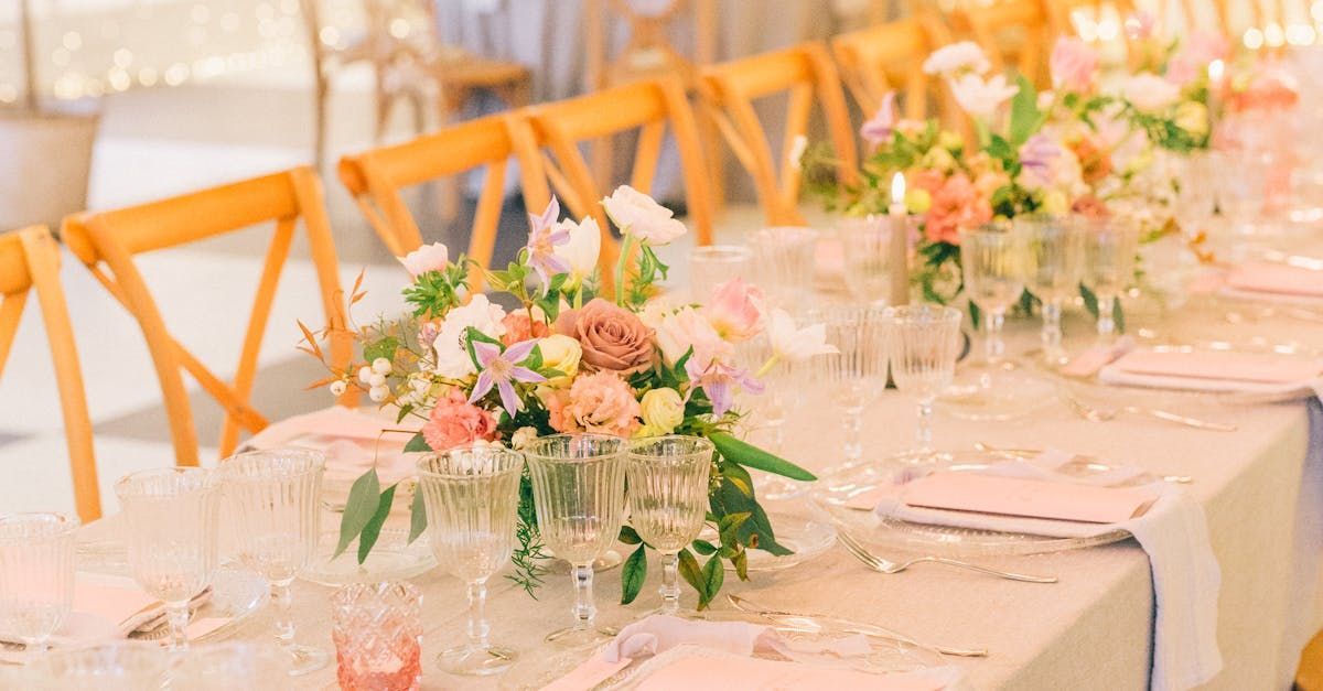 Elegant wedding reception table set with floral centerpieces, glasses, and pink napkins.