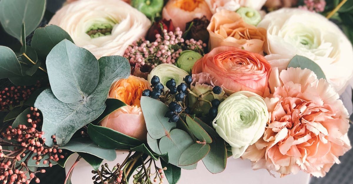Floral arrangement with soft pink, orange, and white blooms, accented by blue-green foliage and berries.