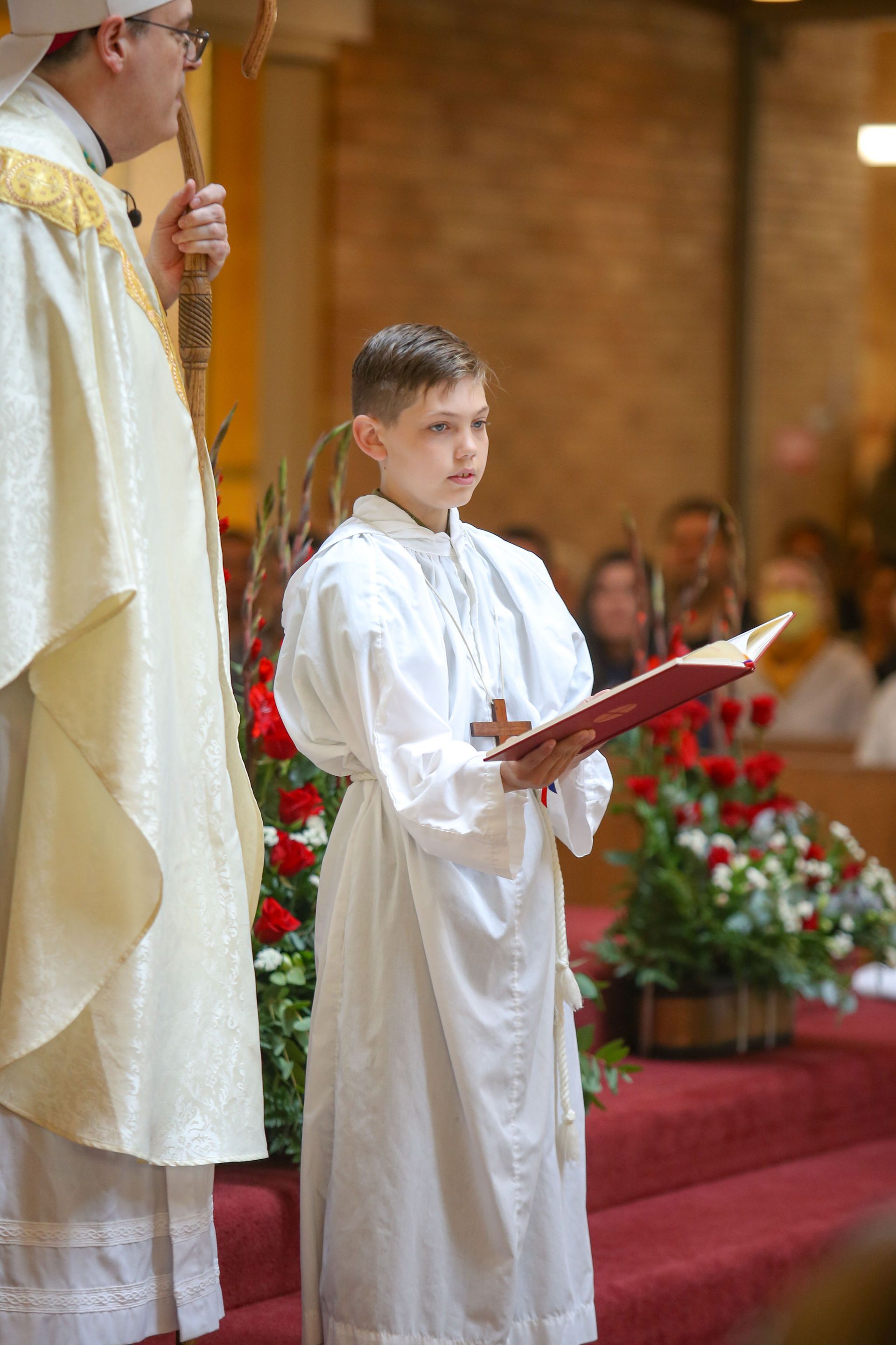 Young altar server in white robe holding a book during a church ceremony