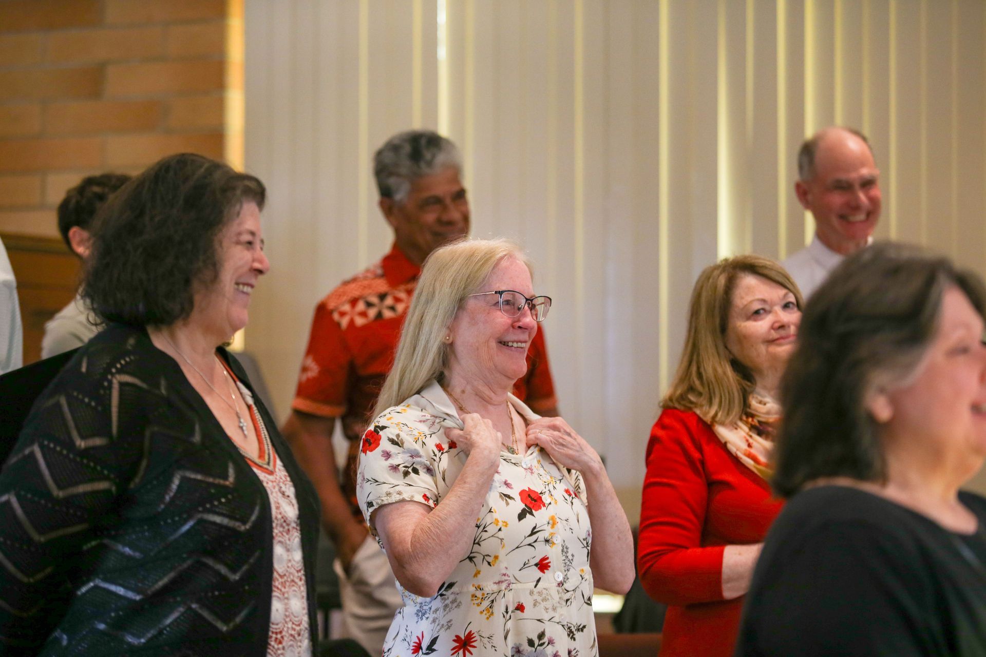 Smiling people standing indoors at an event, one woman in a floral shirt in the foreground