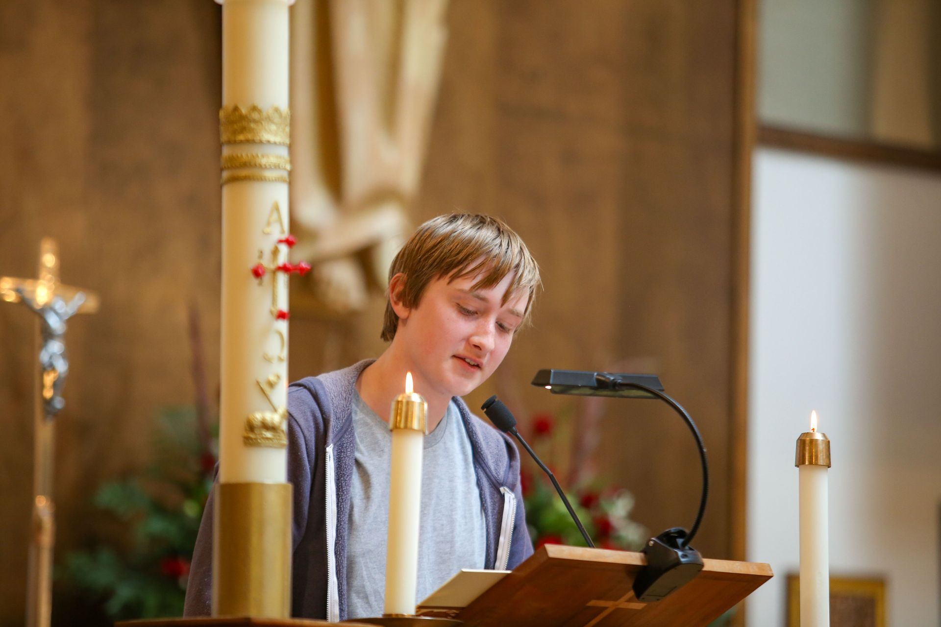 Person speaking at a lectern in a church, with candles and a microphone nearby.