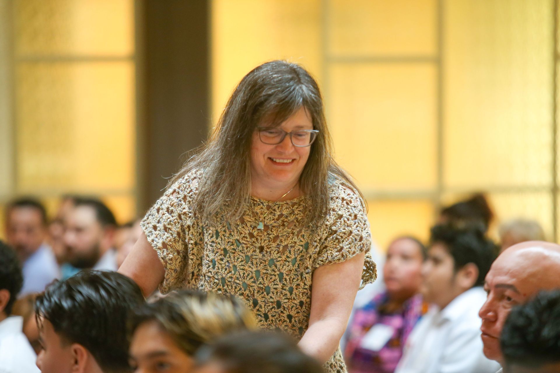 Smiling woman  in patterned blouse standing over mass attendees