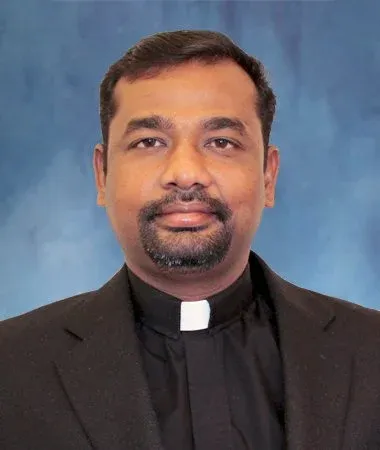 Father Albert  in a black clerical shirt with white collar, against a blue background