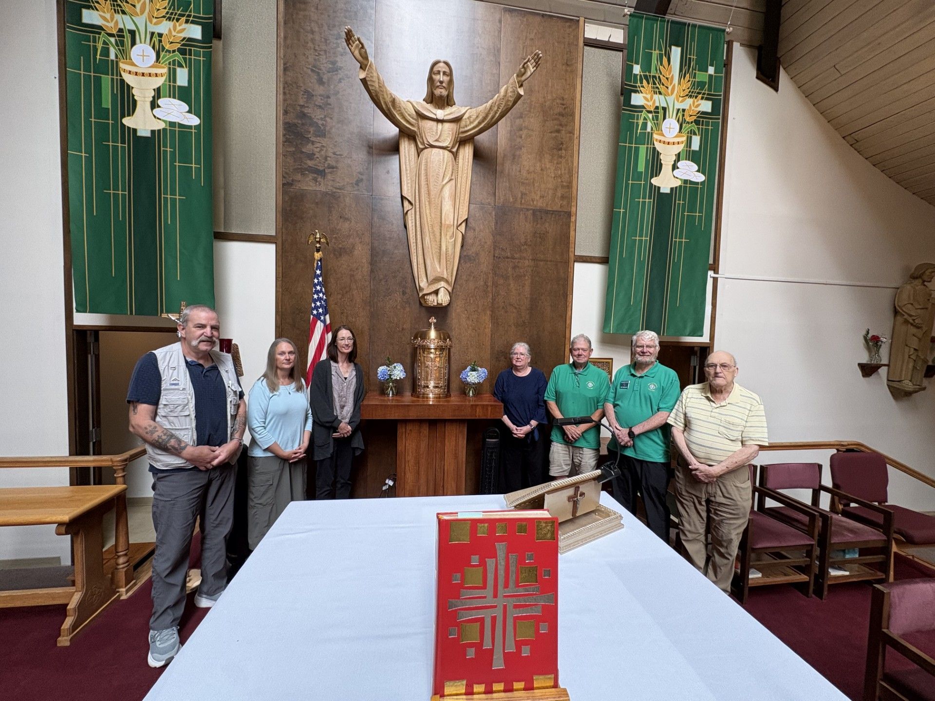 Group standing in a church sanctuary behind a red altar cloth and under a large crucifix statue.