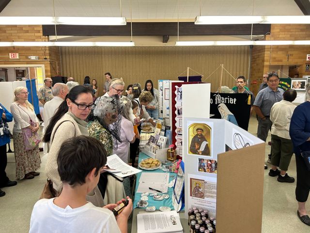 Crowd indoor fair with people browsing posters and displays at a table.