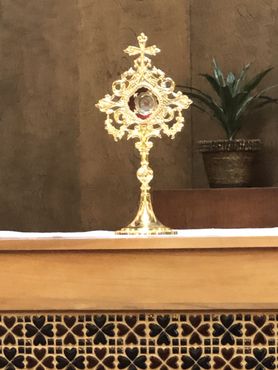 Gold ornate monstrance on a wooden altar with a potted plant in the background