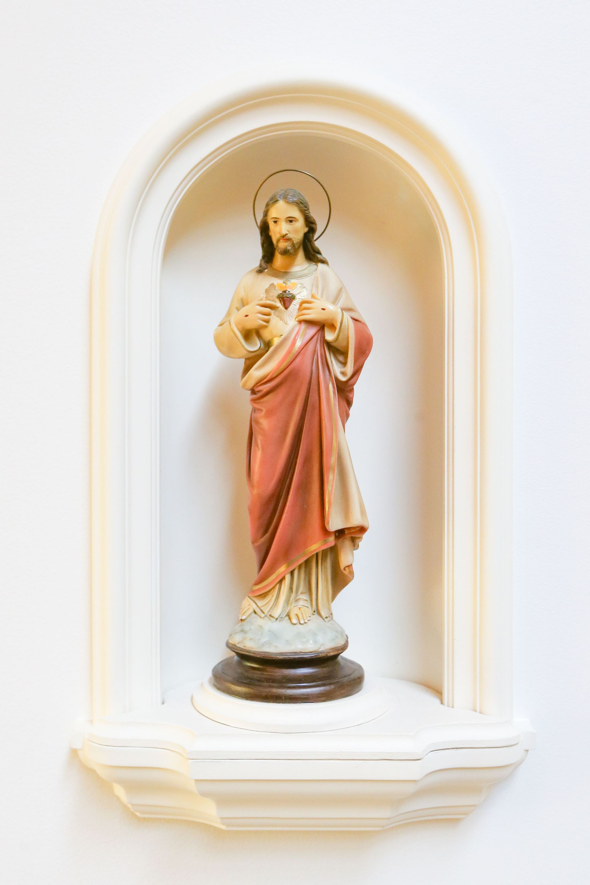 Statue of Jesus in a white wall niche, wearing a pink robe and holding his sacred heart.