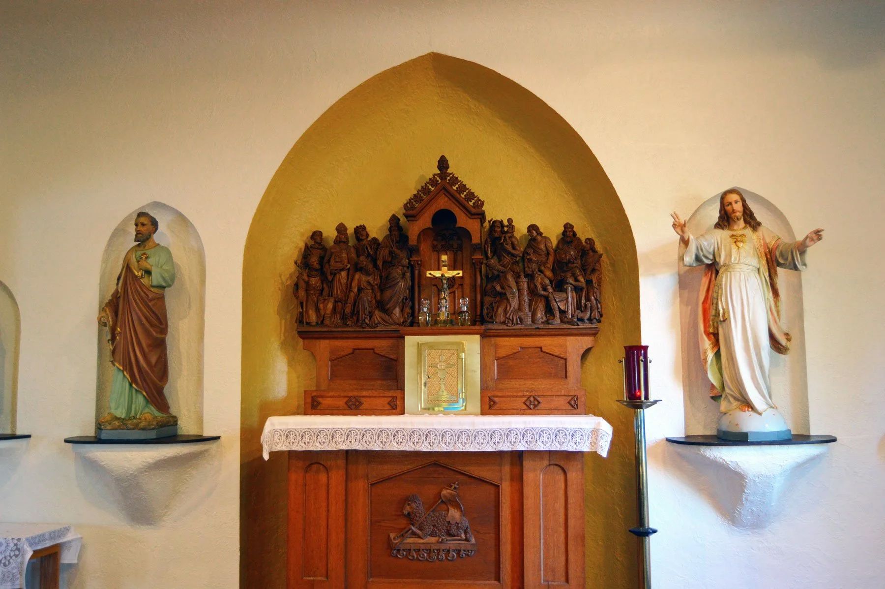 Church altar with statues on either side and a carved wooden tabernacle under a yellow arch