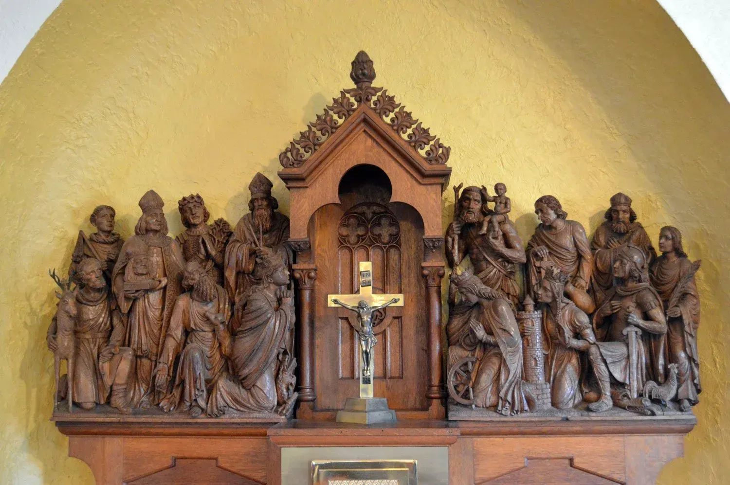 Wooden religious sculpture with crucifix centered, flanked by carved saints on a gold arched altar backdrop