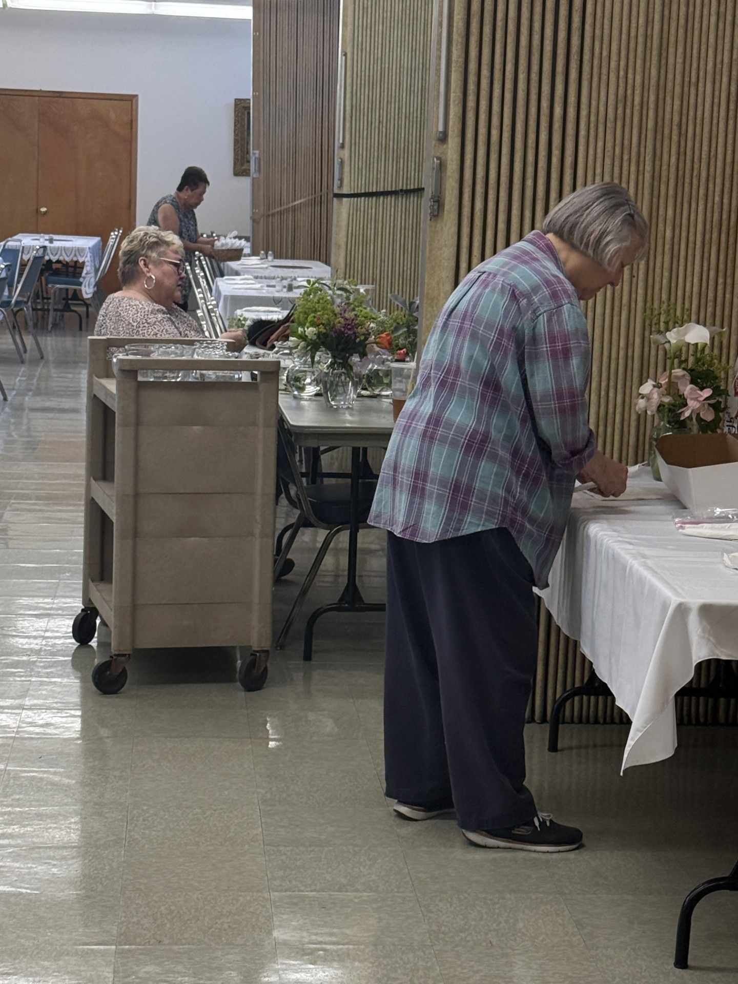 People arranging flowers at a table in a hall or community room.