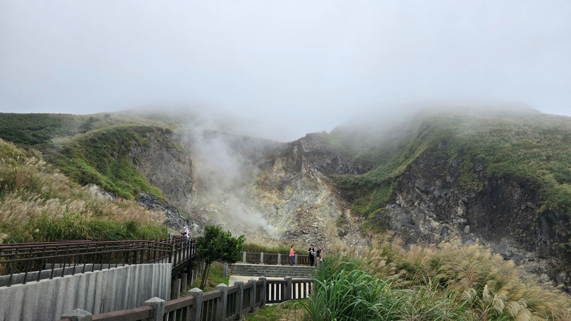 霧氣瀰漫的山景,一條木棧道蜿蜒而上;中心區域蒸汽裊裊升起;隱約可見一些人影。