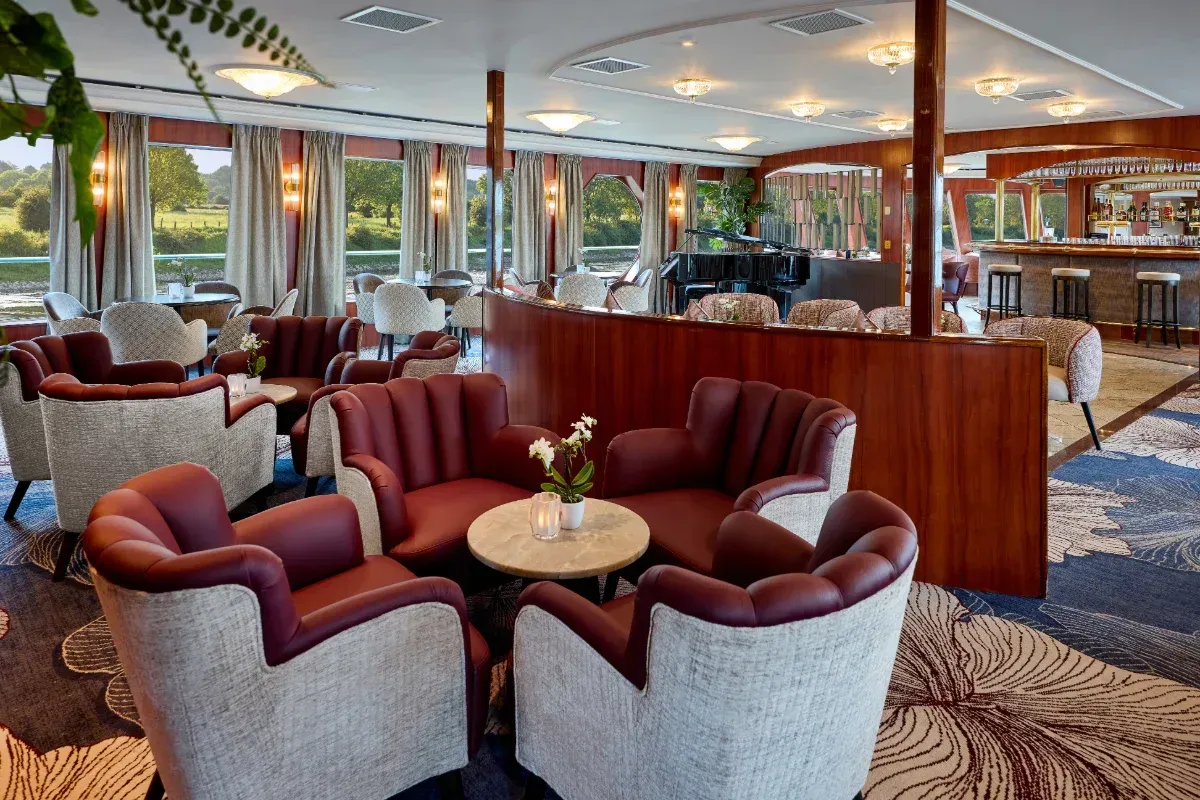 Modern hotel lounge with red armchairs, round tables, and large windows overlooking greenery.