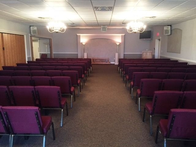 Empty small chapel with rows of burgundy chairs facing a front stage and pulpit