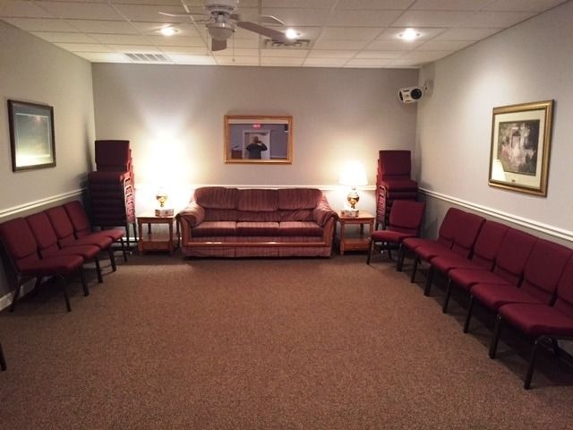 Waiting room with maroon chairs along the walls, a brown sofa, lamps, and framed artwork.