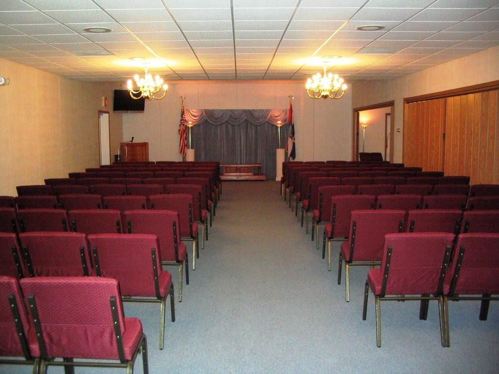Empty banquet hall with rows of red chairs facing a small stage and curtains