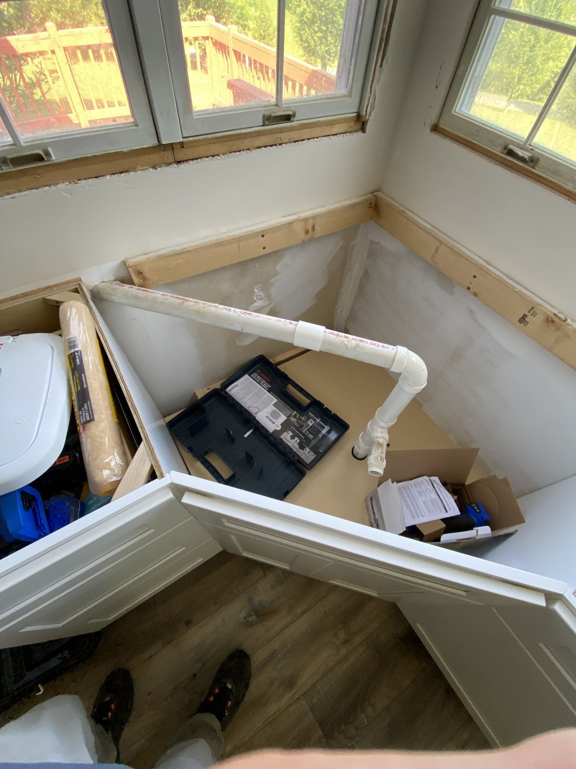 A partially constructed storage space with exposed framing and a PVC pipe, near a window.