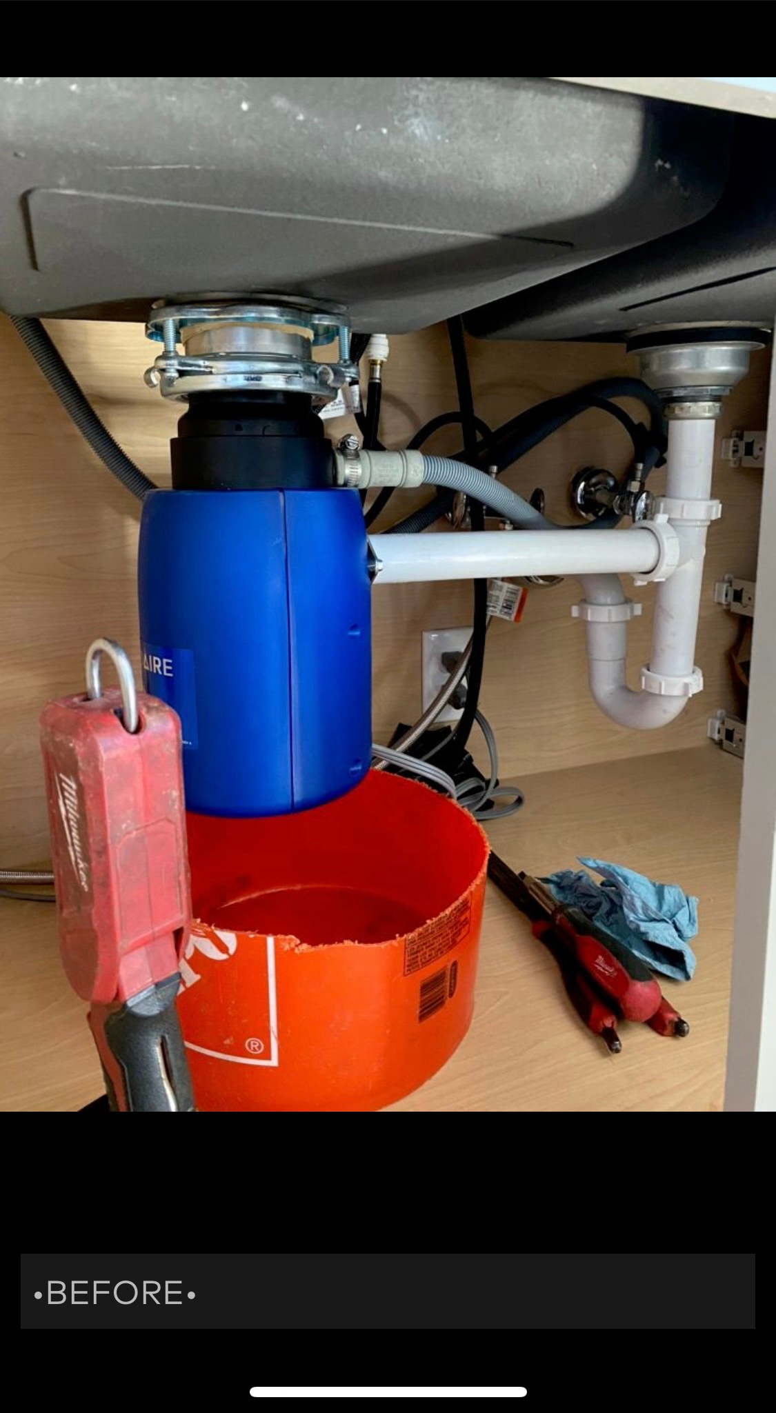 Garbage disposal unit under a kitchen sink. Blue and red containers, white pipes.