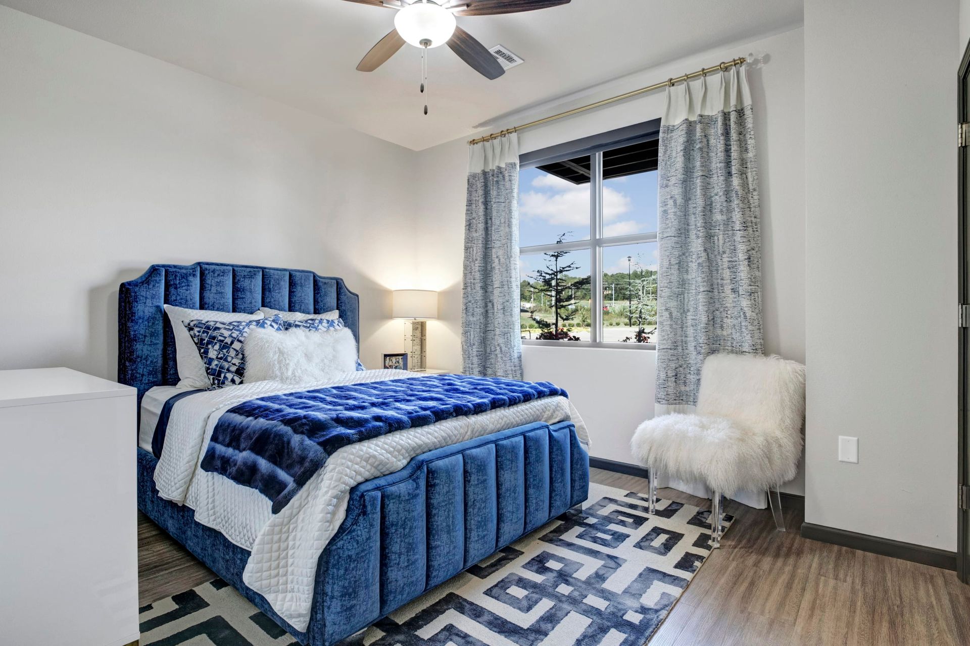 A bedroom with a bed , chair , rug and ceiling fan.