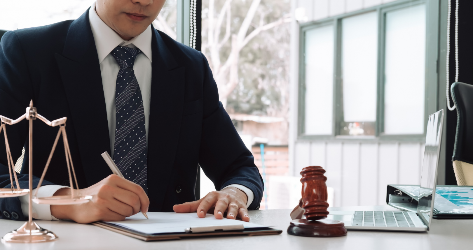 View our Service Area Lawyer writing at desk with gavel and scales of justice in a bright office