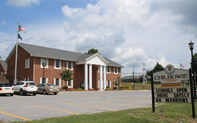 Brick school building with parking lot and sign reading “CHILHOWIE,” under a partly cloudy sky.