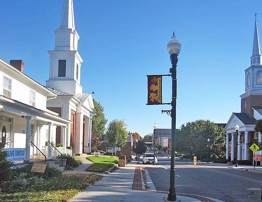 Quiet Downtown Christiansburg street with white church steeples, sidewalk, lamppost, and blue sky.