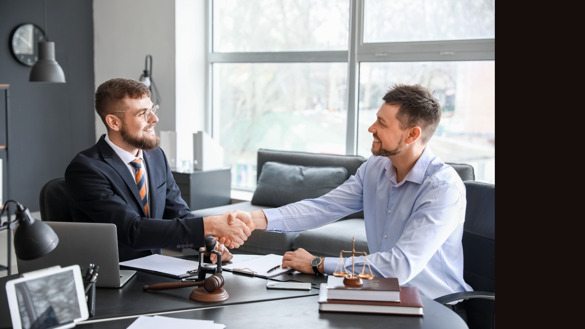 Contact us today! Two men in business attire shaking hands across a desk in a bright office