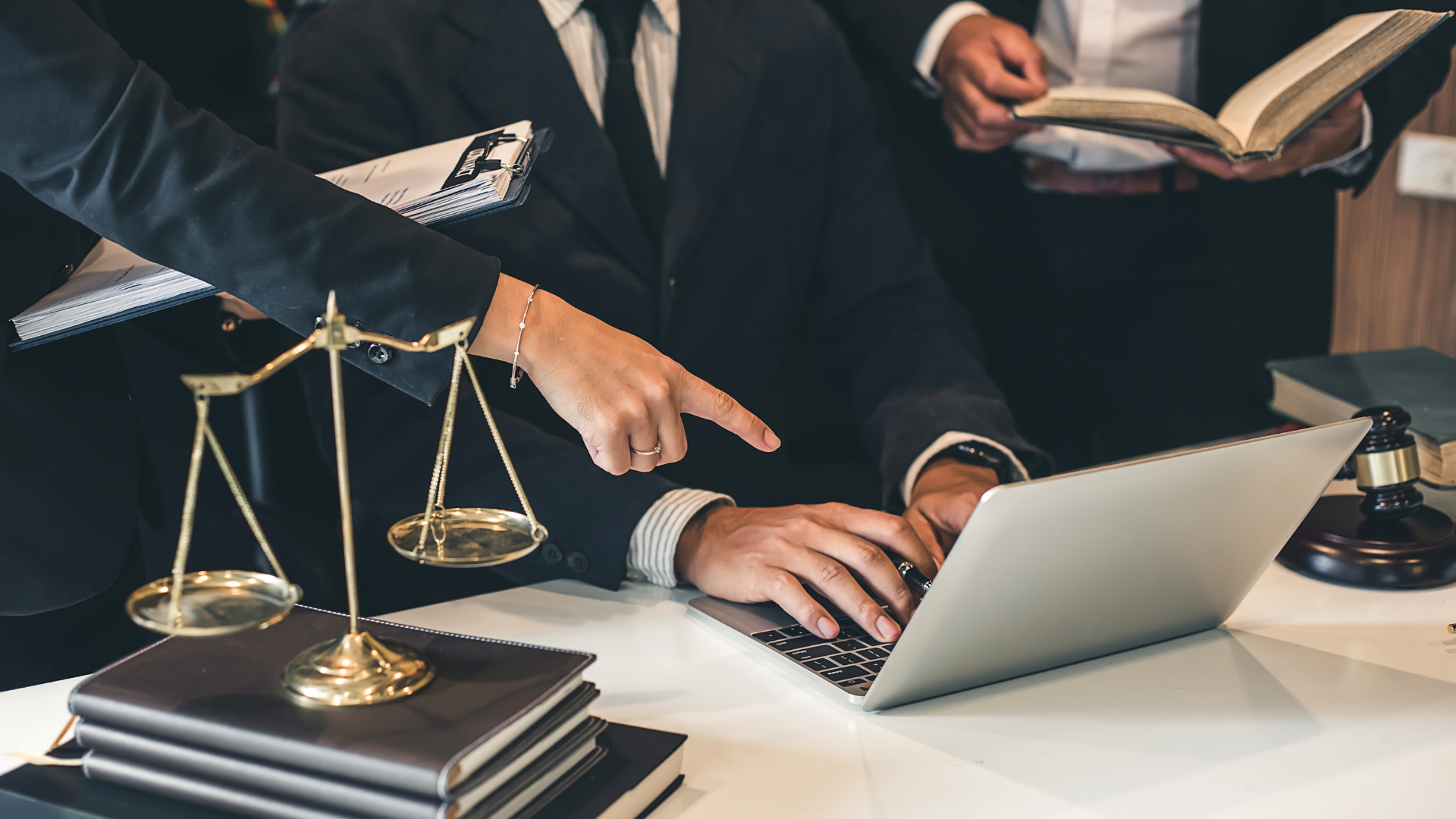 Scope out The Felty Legal Brief Blog. Law office scene with scales of justice, stacked books, and a person typing on a laptop as another holds an open book
