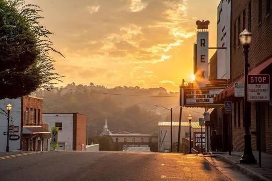 Sunlit empty street at sunset with storefronts, palm trees, and a distant hillside in Galax Virginia