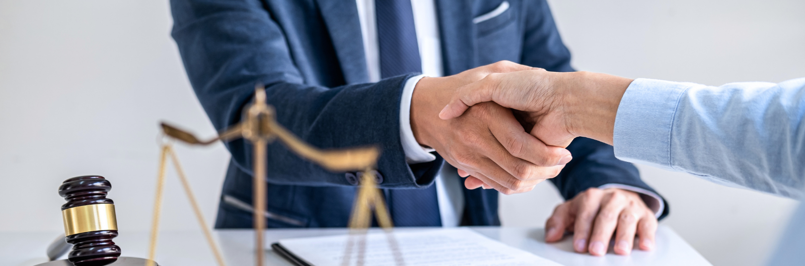 Handshake across a desk in a legal office, with a gavel and scales of justice in the foreground