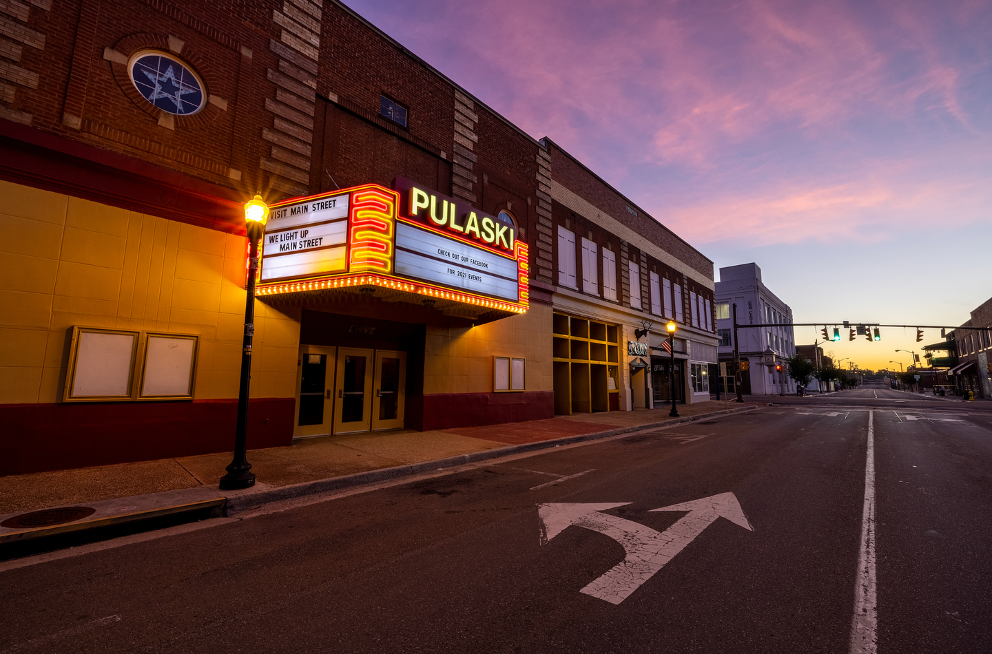 Empty street at dusk with a lit Pulaski theater marquee and purple sunset sky