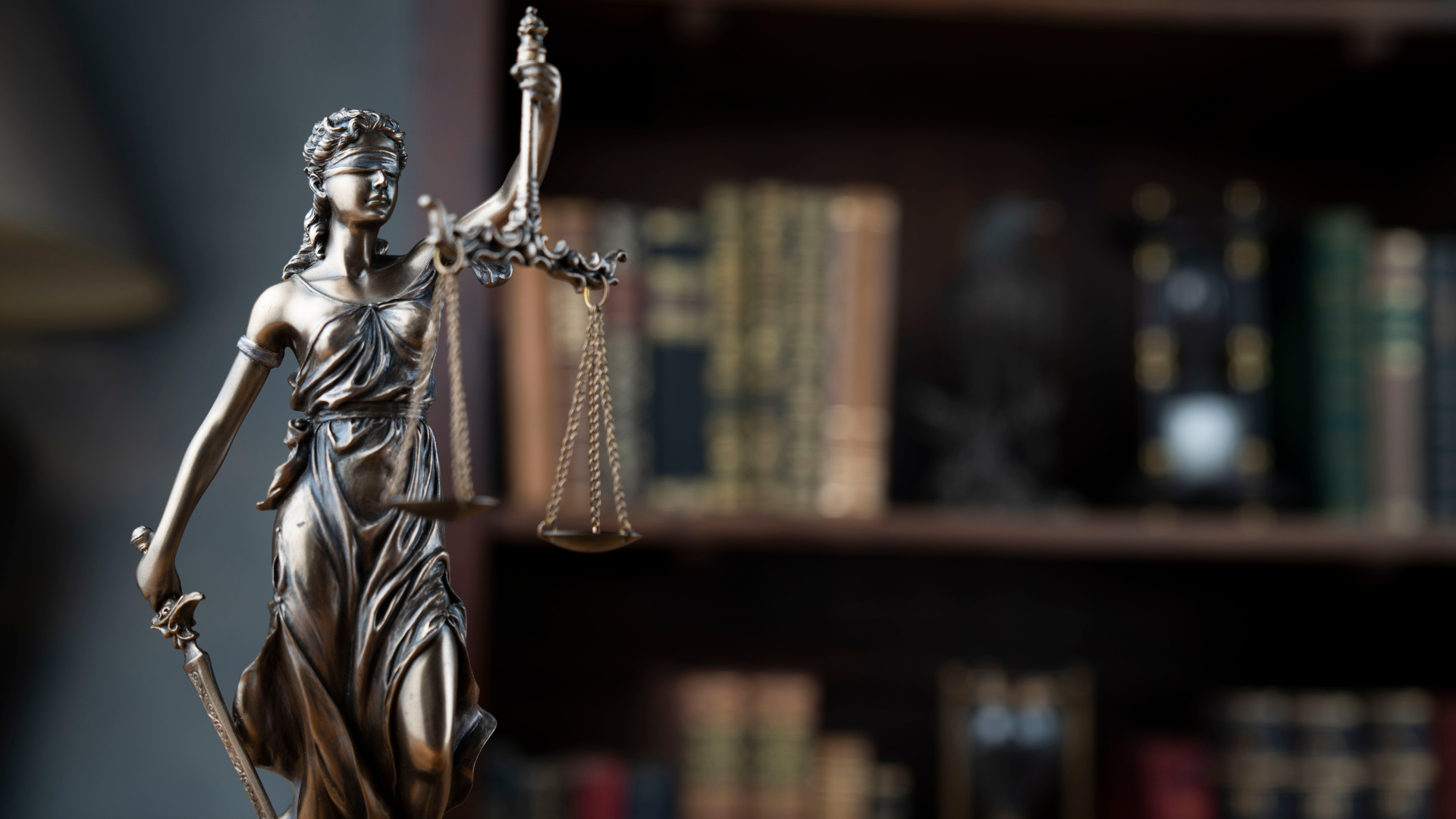 Scope out The Felty Legal Brief Blog. Statue of Lady Justice with scales in front of blurred law books