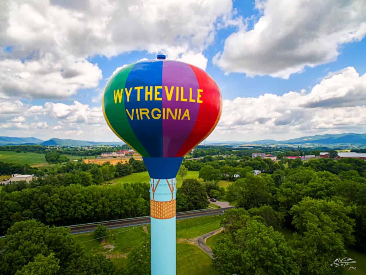 Colorful hot air balloon reading “Wytheville Virginia” floating above green fields and trees under a cloudy sky