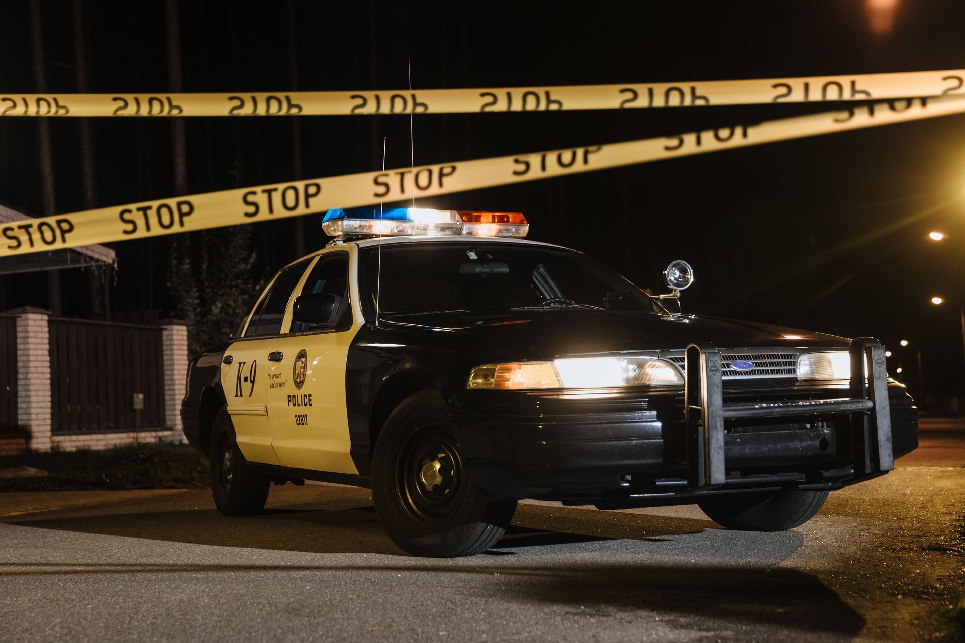 Police car behind yellow crime scene tape at night on a dimly lit street