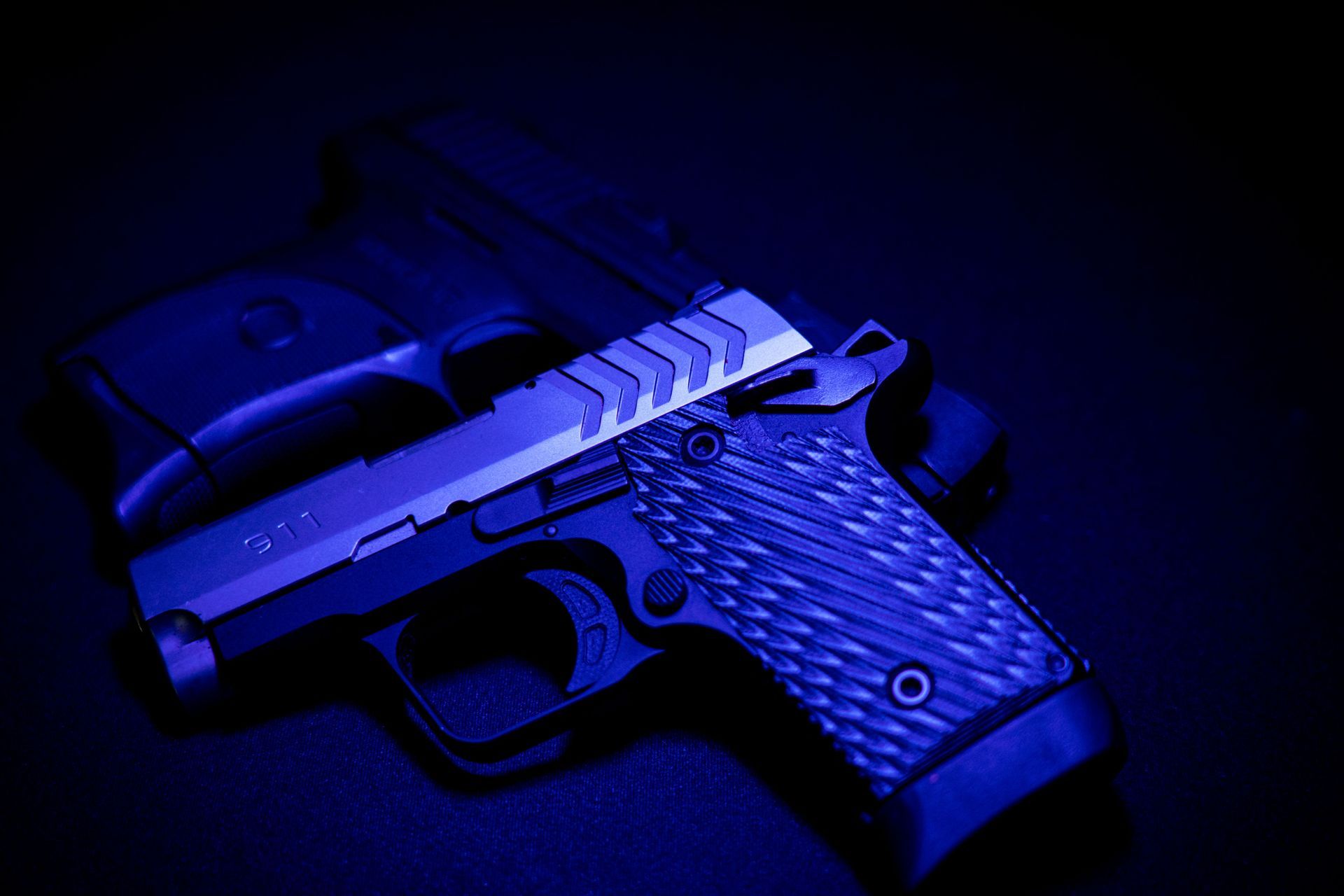 Blue-lit handgun on a dark surface, shown in close-up.