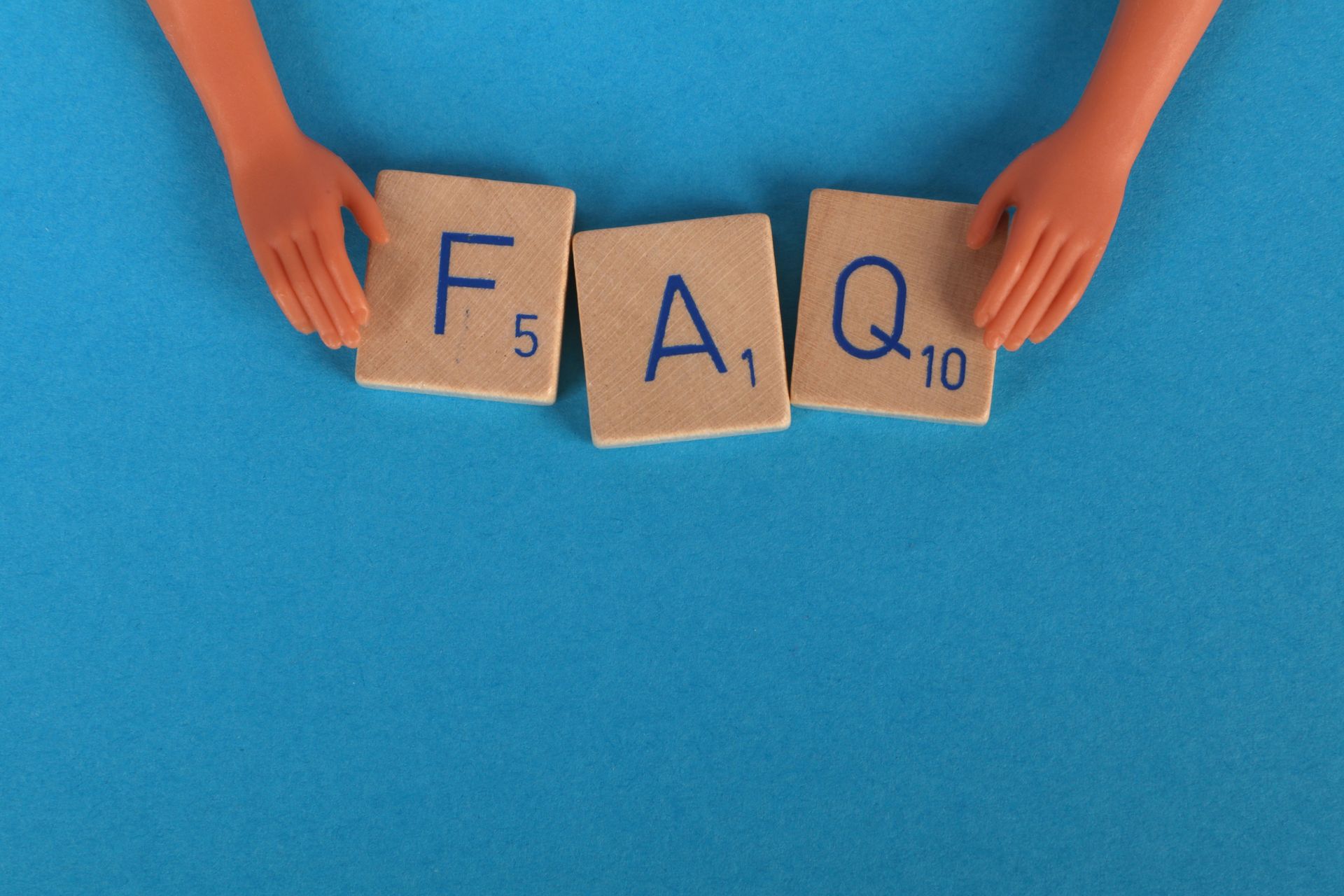 Hands holding wooden letter tiles spelling “FAQ” on a blue background.