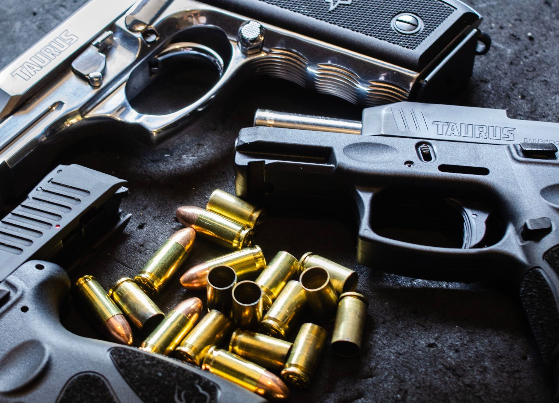 Assorted firearms laid out on a wooden table beside a woven chair in a dark room