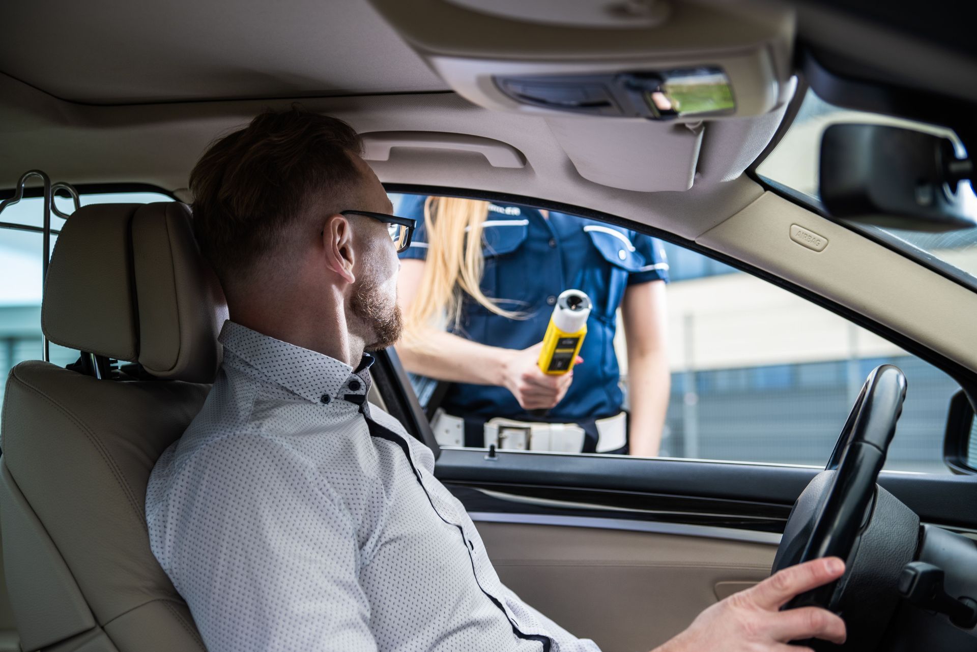 Driver at a roadside checkpoint speaking to an officer holding a breathalyzer outside the car window